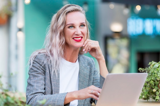 Giovane donna sorridente con un laptop in un bellissimo caffè di strada lavoro a distanza e freelance