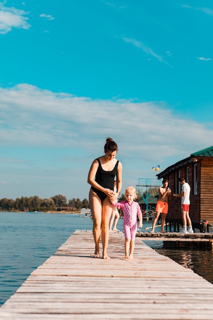 Young smiling woman with little girl kid at wooden pier at lake beach summer time