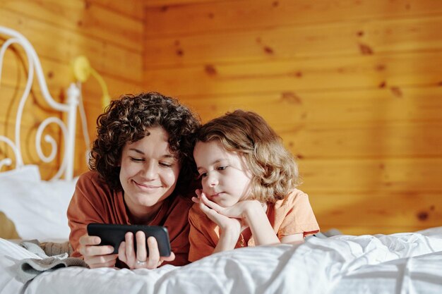 Young smiling woman with mobile phone and her son watching movie