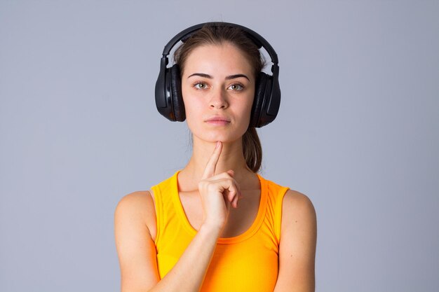 Young smiling woman with ponytail in yellow Tshirt and headphones on gray background in studio