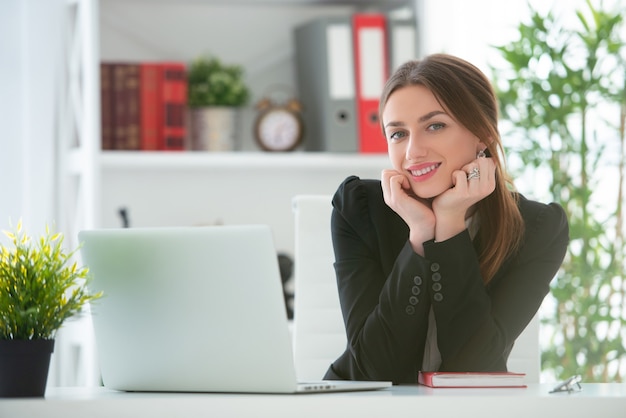 Young smiling woman working at a desk with a laptop in an office