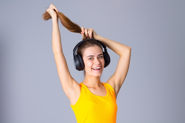 Young smiling woman in yellow Tshirt listening to the music in black headphones in studio