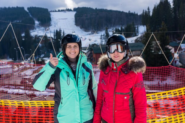 Foto giovani donne sorridenti in tute da sci, con caschi e occhiali da sci in piedi in una stazione sciistica nel periodo invernale