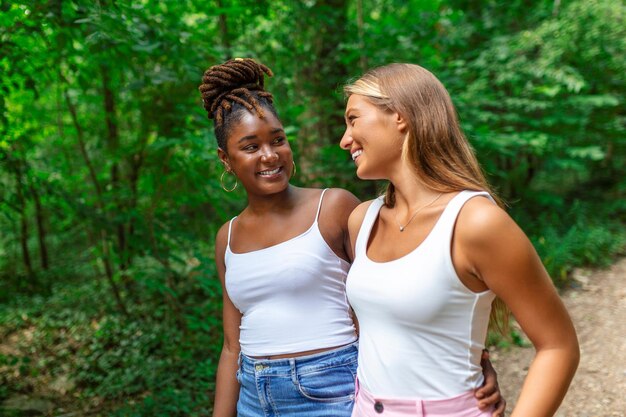 Young smiling women walking and talking while looking at each other outdoor Happy best friends laughing and having funTwo women friends sightseeing in summer while on vacation