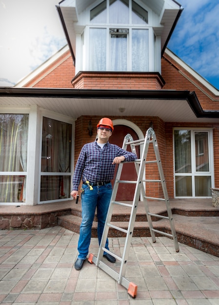 Young smiling worker posing against beautiful newly built house