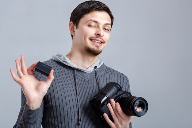 Young smilling photographer in shirt holds the battery for DSLR