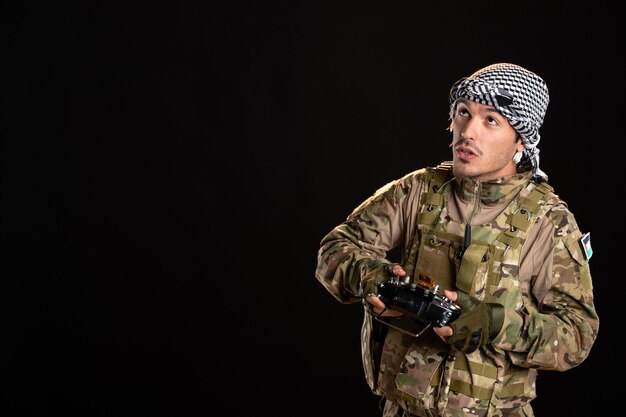 Young soldier in camouflage using remote controller on a black wall