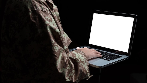 Photo young soldier working with a laptop computer with blank screen on black background