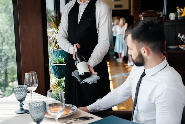 Un giovane sommelier in elegante divisa fa una dimostrazione e offre al cliente un buon vino nel ristorante servizio clienti allestimento tavola in un raffinato ristorante