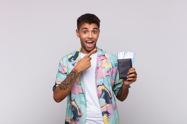 Young south american man looking excited and surprised pointing to the side and upwards to copy space