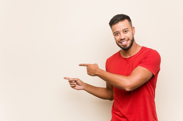 Young south-asian man excited pointing with forefingers away.