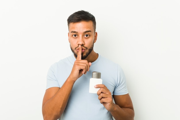 Young south-asian man holding an after shave cream keeping a secret or asking for silence.