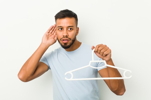 Young south asian man holding a hanger trying to listening a gossip