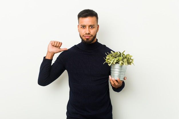 Young south-asian man holding a plant feels proud and self confident