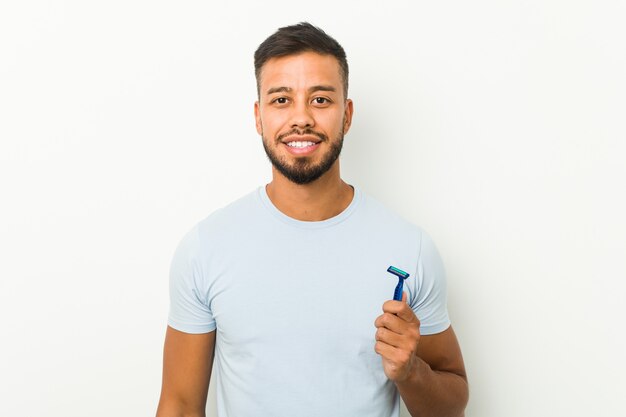 Young south-asian man holding a razor blade happy, smiling and cheerful.