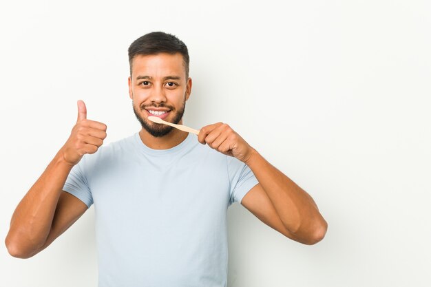 Young south-asian man holding a toothbrush smiling and raising thumb up