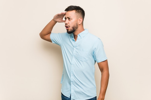 Young south-asian man looking far away keeping hand on forehead.