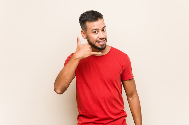 Young south-asian man showing a mobile phone call gesture with fingers.