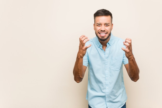 Young south-asian man upset screaming with tense hands.