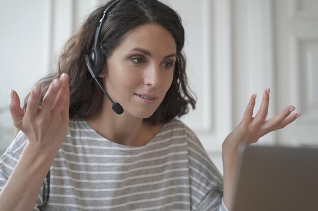 Giovane donna di affari spagnola che indossa le cuffie senza fili che consulta il cliente in linea