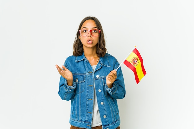 Young spanish woman holding a flag isolated on white wall surprised and shocked.