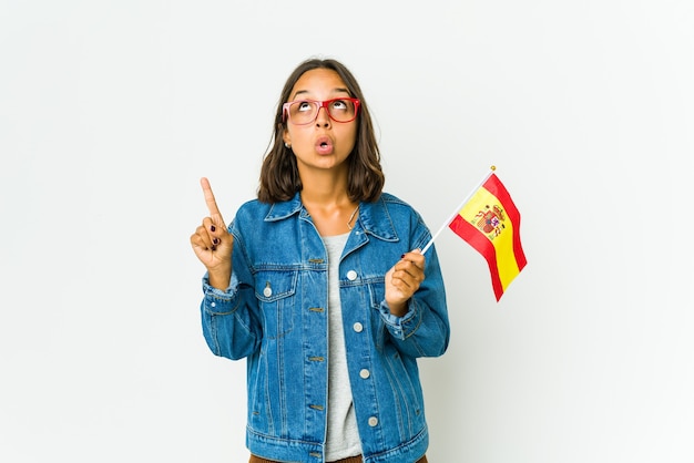 Young spanish woman holding a flag pointing upside with opened mouth