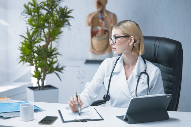 A young specialist doctor is sitting at a table in his bright office