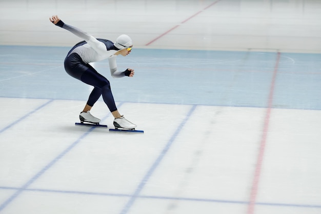 Young speed skater with legs bent in knees and right arm stretched behind back