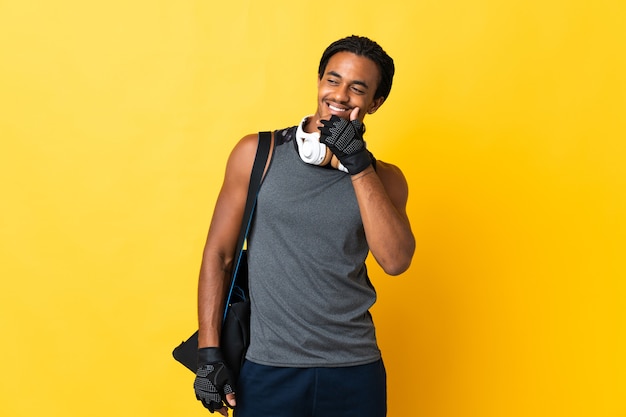 Young sport African American man with braids with bag isolated on yellow background happy and smiling