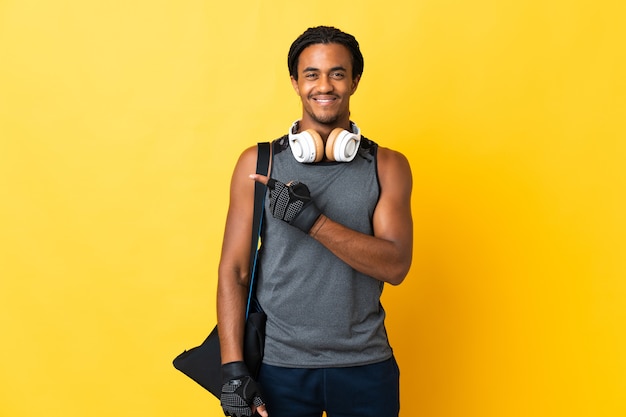 Young sport African American man with braids with bag isolated on yellow background pointing to the side to present a product