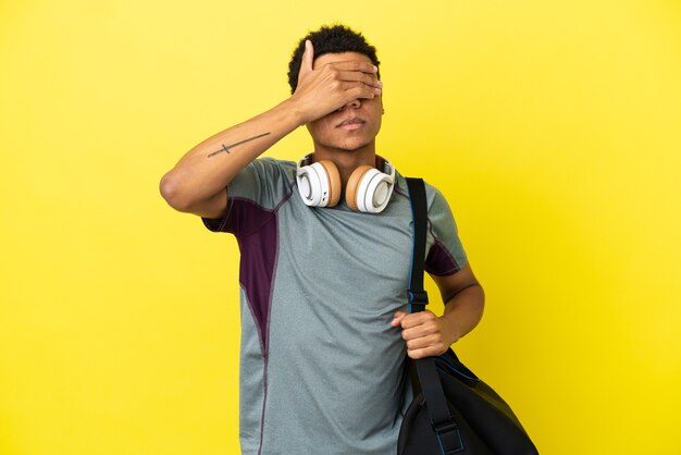 Young sport African American man with sport bag isolated on yellow background covering eyes by hands. Do not want to see something