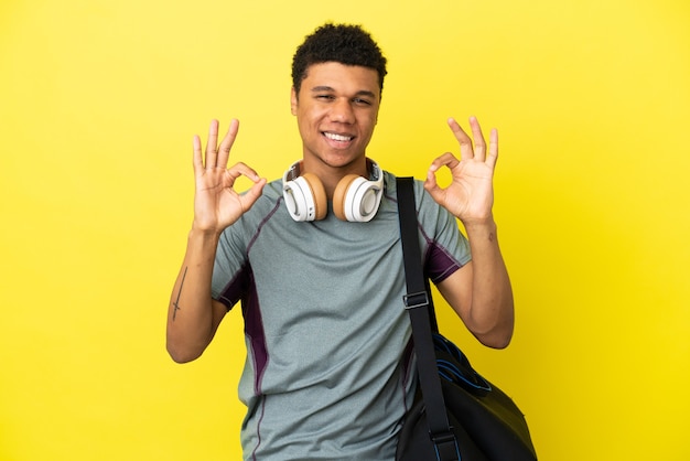 Young sport African American man with sport bag isolated on yellow background showing an ok sign with fingers