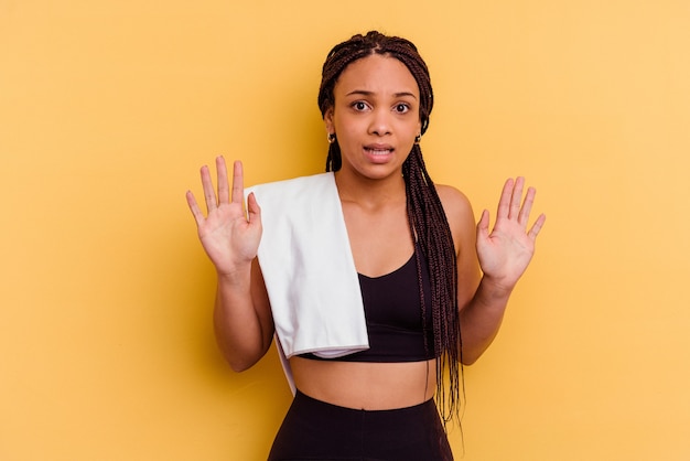 Young sport african american woman holding a towel isolated on yellow background rejecting someone showing a gesture of disgust.