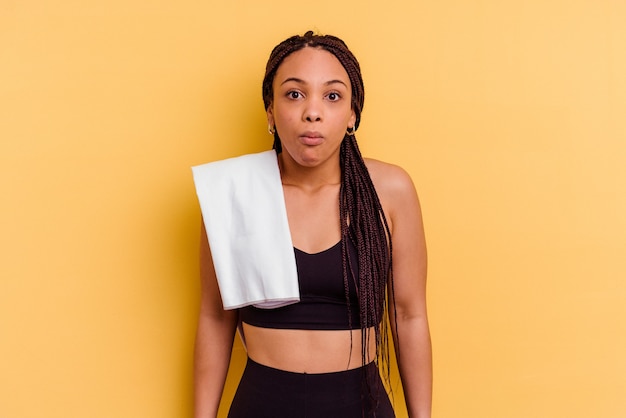 Young sport african american woman holding a towel   shrugs shoulders and open eyes confused.