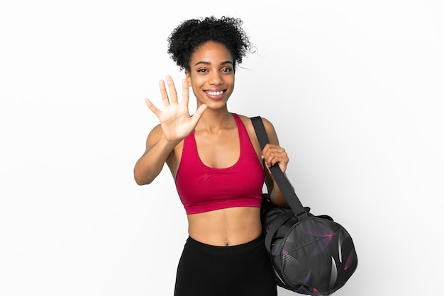Молодая спортивная афро-американская женщина со спортивной сумкой, изолированной на синем фоне, считая пять пальцами