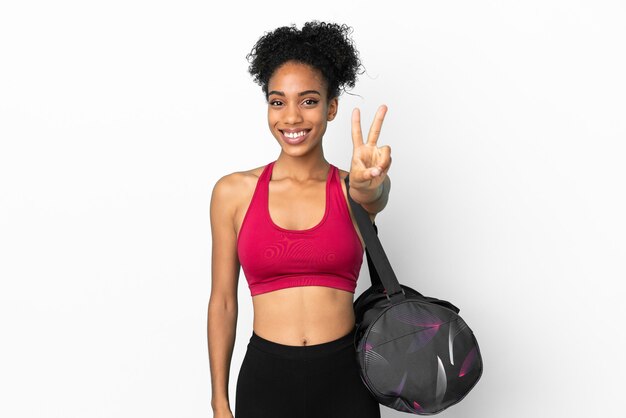 Young sport african american woman with sport bag isolated on blue background smiling and showing victory sign