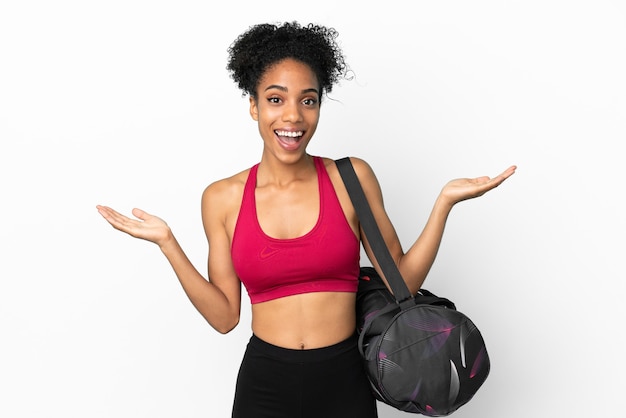 Молодая спортивная афро-американская женщина со спортивной сумкой на синем фоне с шокированным выражением лица