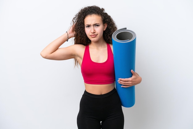 Young sport Arab woman going to yoga classes while holding a mat isolated on white background having doubts