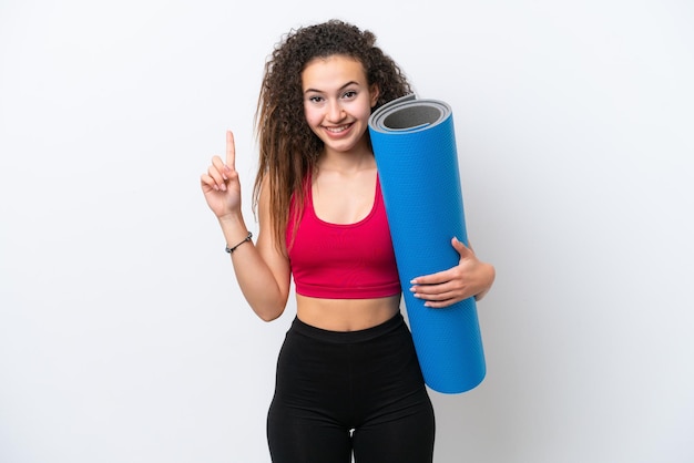 Photo young sport arab woman going to yoga classes while holding a mat isolated on white background showing and lifting a finger in sign of the best