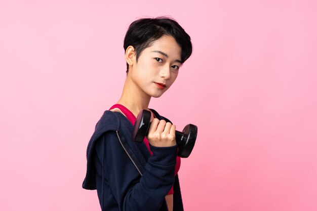 Young sport Asian woman over isolated pink wall making weightlifting