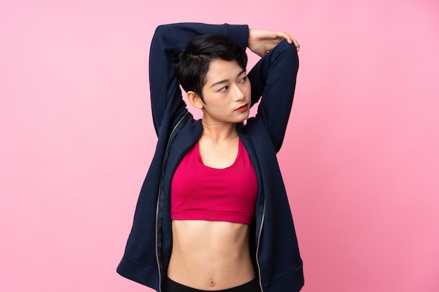 若いスポーツアジア女性の孤立したピンクの壁のストレッチ