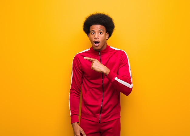 Young sport black man over an orange wall pointing to the side