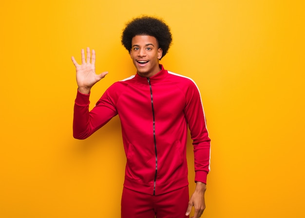 Young sport black man over an orange wall showing number five