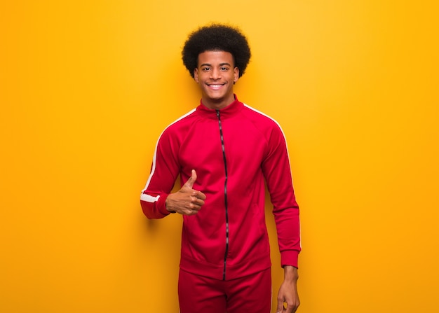 Young sport black man on an orange wall smiling and raising thumb up