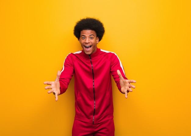 Young sport black man over an orange wall very happy giving a hug to the front