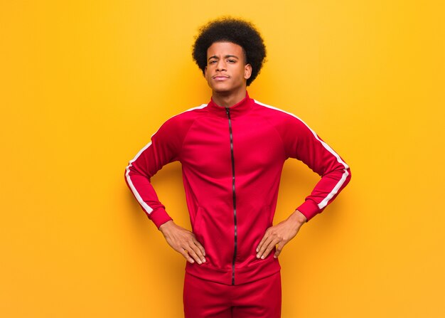 Young sport black man over an orange wall with hands hips