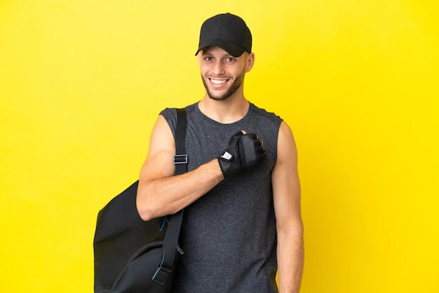 Young sport blonde man with sport bag isolated on yellow background celebrating a victory