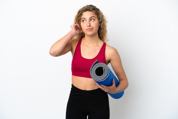 Young sport blonde woman going to yoga classes while holding a mat isolated on white background having doubts