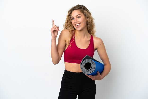 Young sport blonde woman going to yoga classes while holding a mat isolated on white background showing and lifting a finger in sign of the best