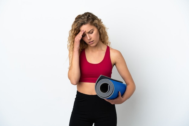 Young sport blonde woman going to yoga classes while holding a mat isolated on white background with headache